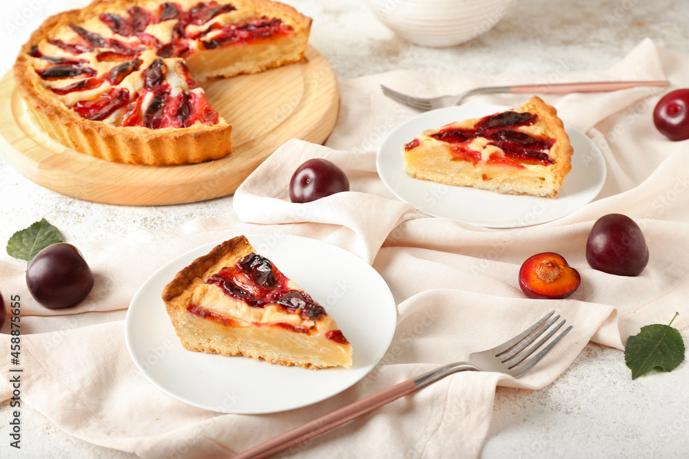 Plates with pieces of tasty plum pie on light background