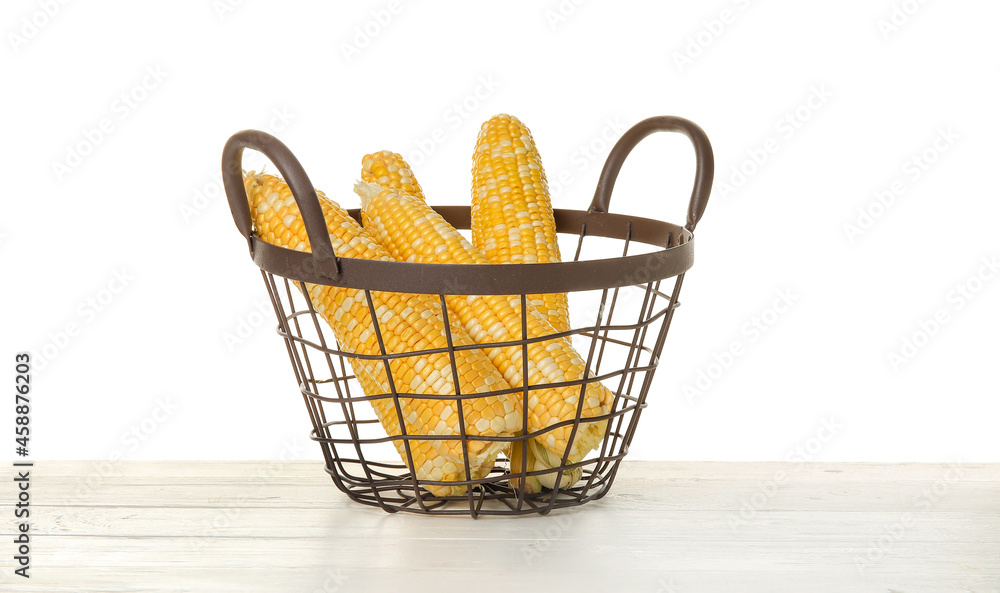 Basket with fresh corn cobs on table against white background