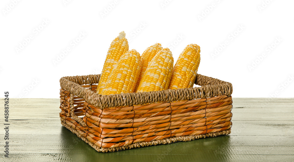 Wicker basket with fresh corn cobs on table against white background