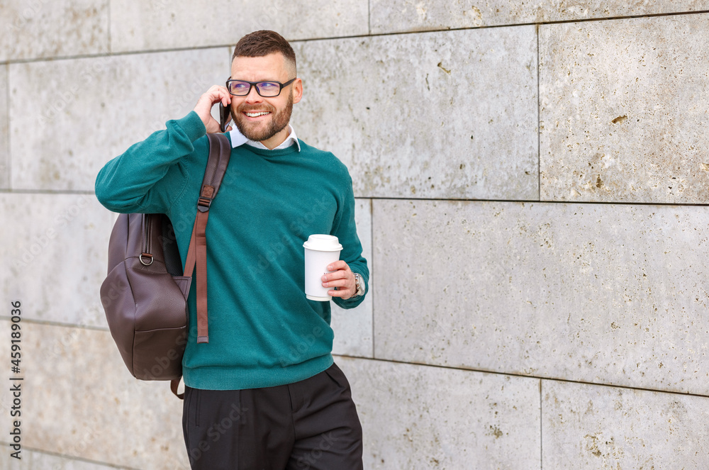 Young happy office worker employee outside speaking on mobile phone with take away coffee in hand