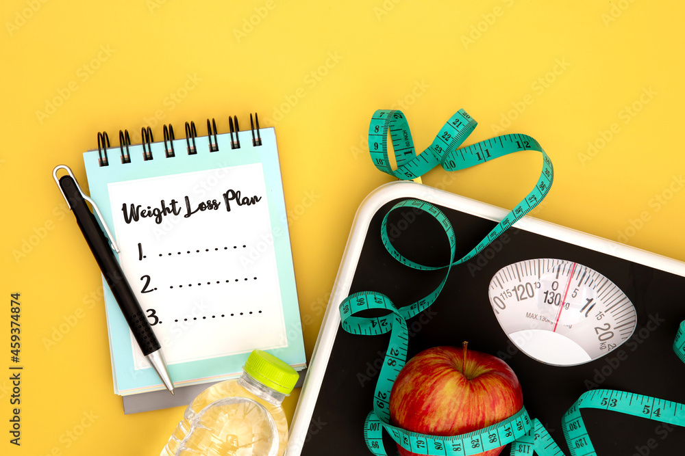 Weight scale and measure tape with fresh apple and notepad paper with handwriting motivation text We