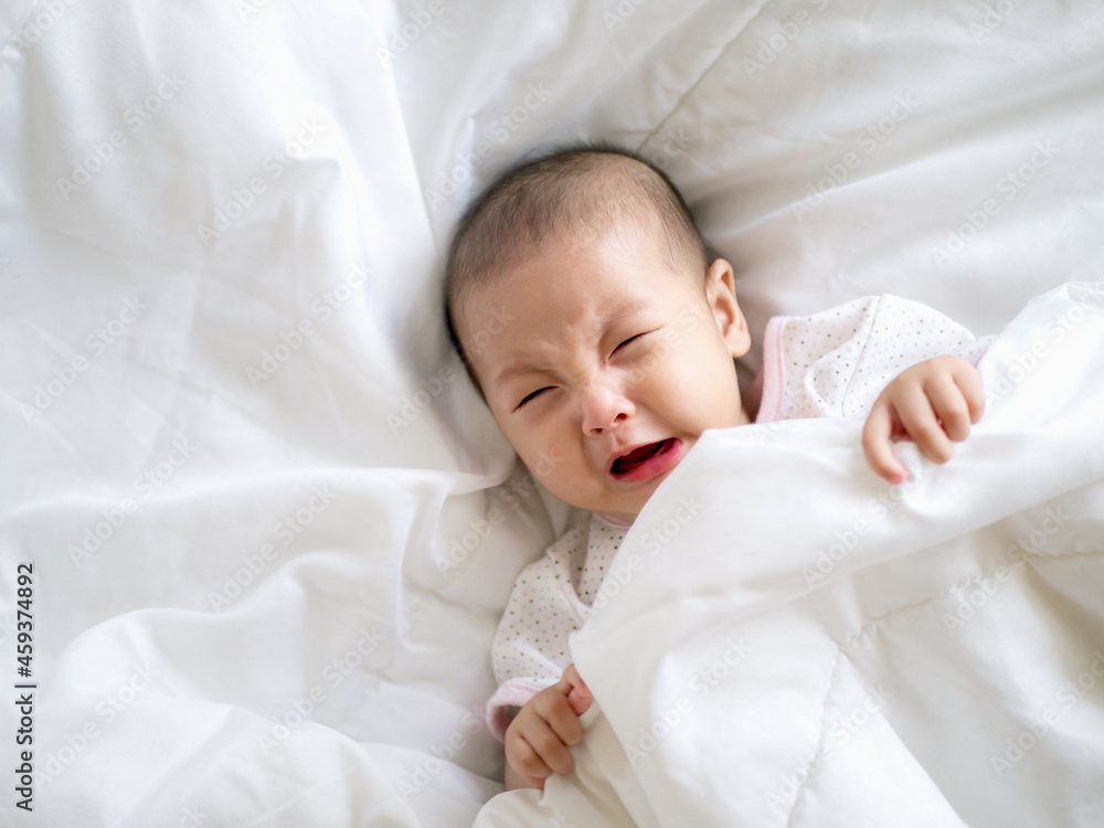 Close up Adorable Asian baby infant girl cry on a white bed , colic symptom or hungry unhappy of inf