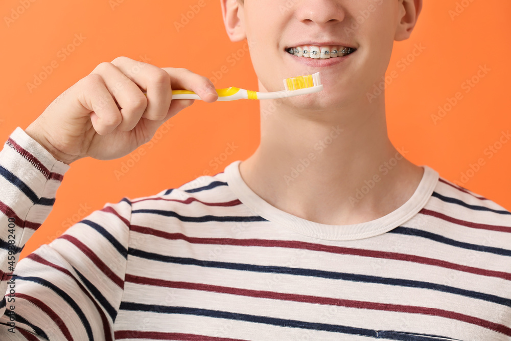 Handsome man with dental braces and toothbrush on color background, closeup