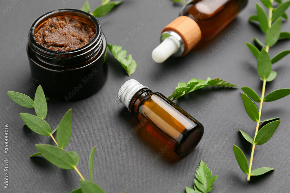 Bottles of healthy essential oil with scrub on dark background