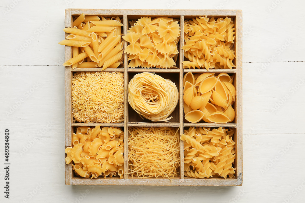 Box with different types of uncooked pasta on white wooden background