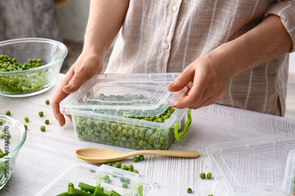 妇女关闭塑料容器，浅背景冷冻豌豆，特写