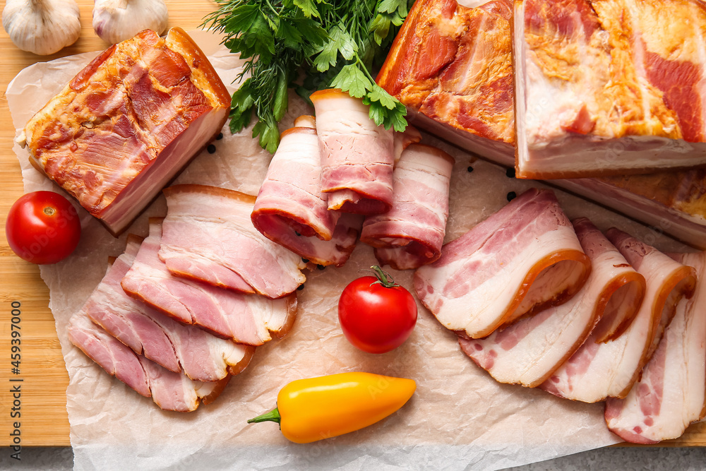 Wooden board with tasty smoked bacon and fresh vegetables on table