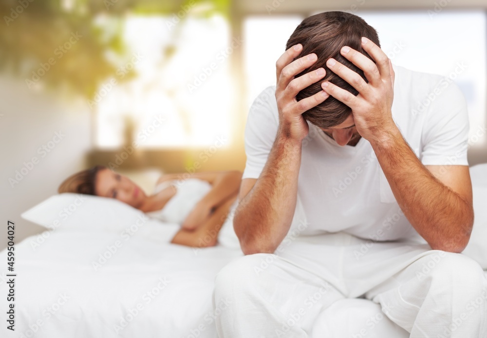 Depressed young man sitting in bed cannot sleep from insomnia