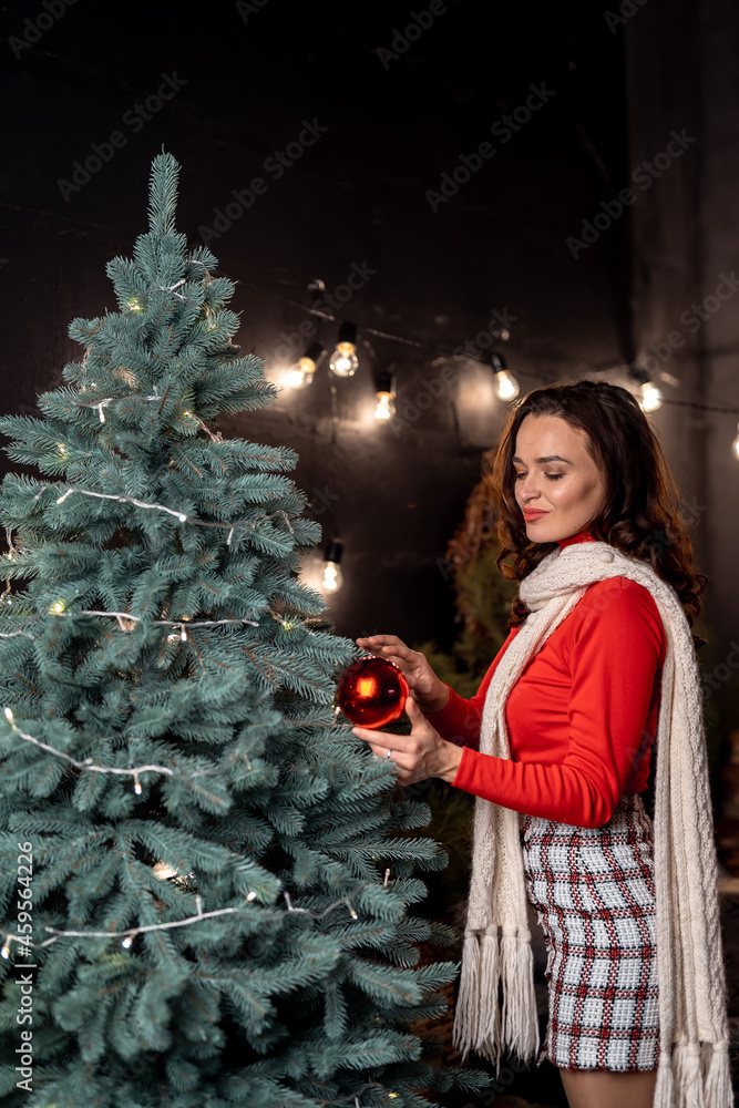 Pretty woman posing to the camera while looking at the ball dreamy standing near the fir tree. Red s