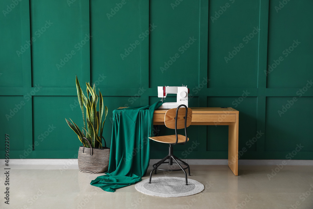 Tailors workplace with sewing machine, cloth and houseplant near green wall