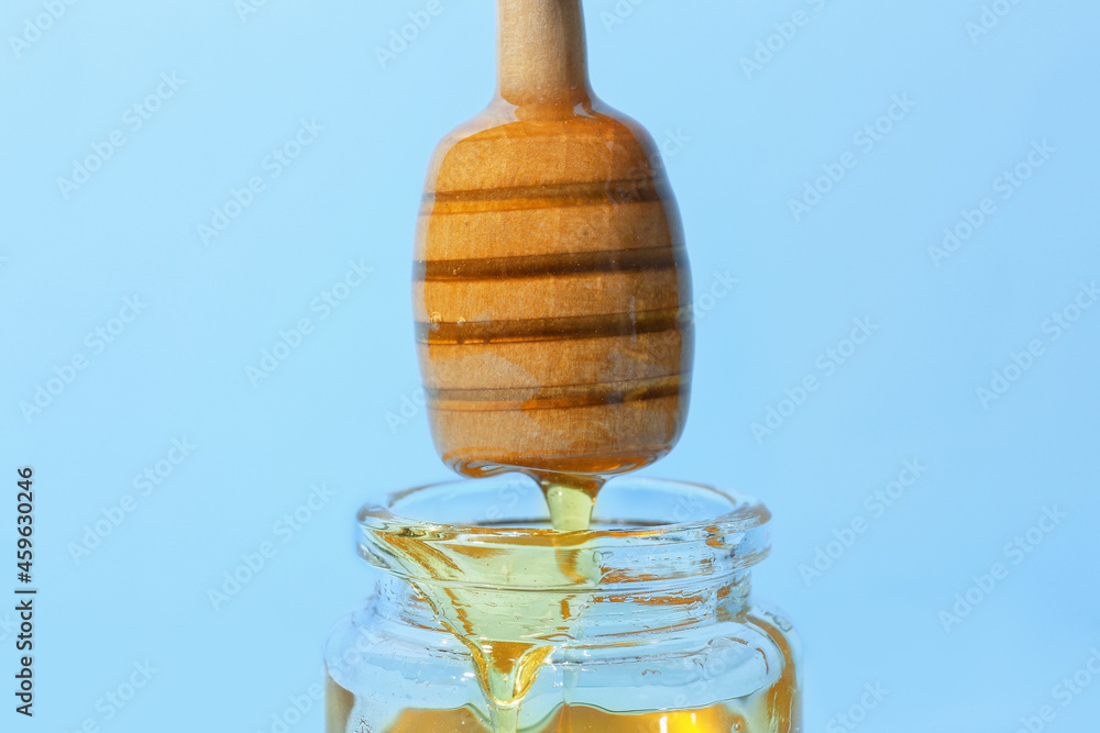 Pouring of sweet honey from dipper on color background, closeup