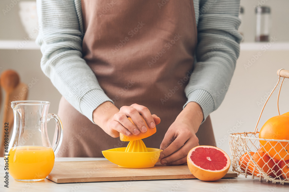 Woman squeezing grapefruit on table in kitchen