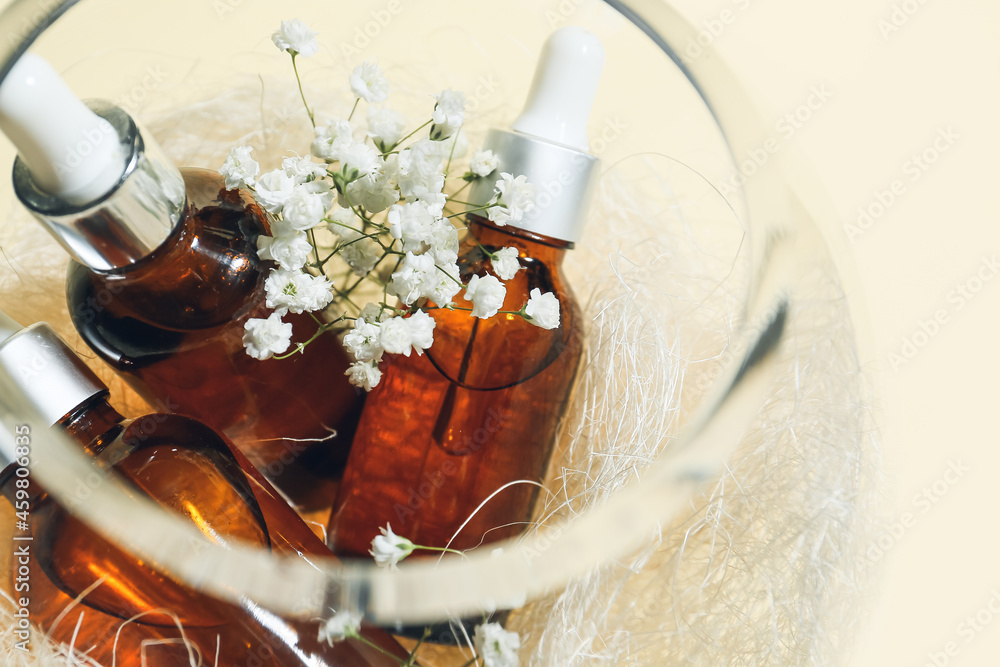 Glass bowl with bottles of healthy essential oil on light background, closeup