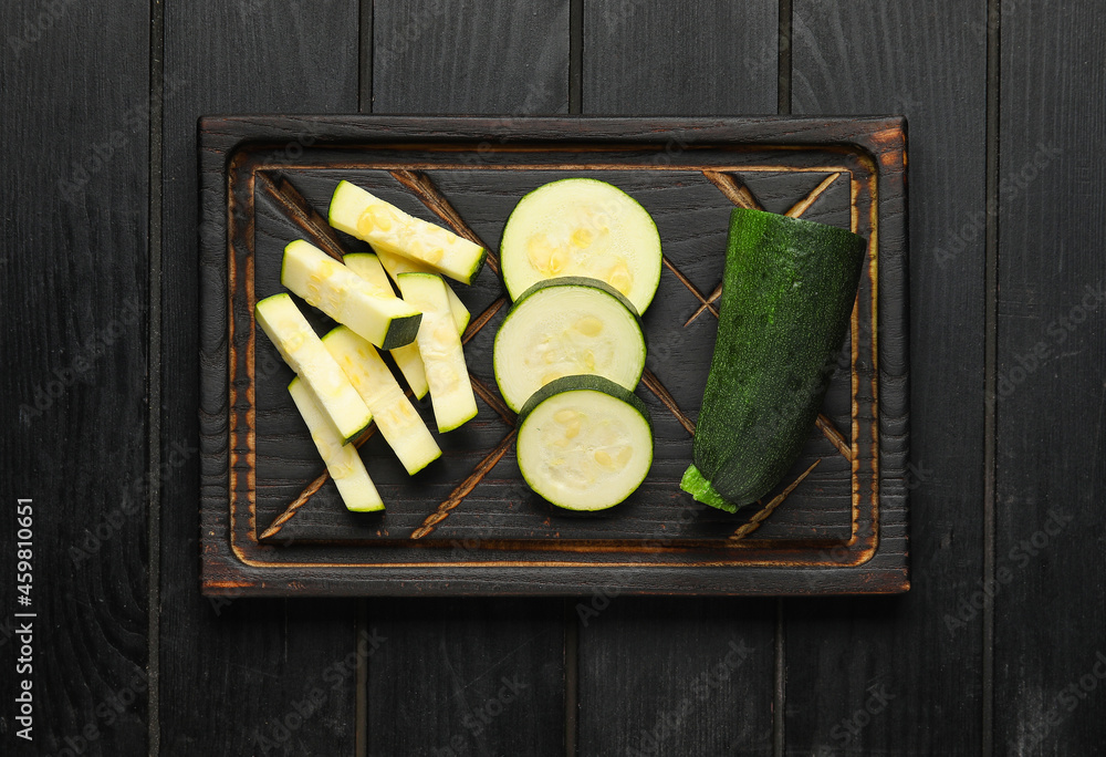 Board with slices of fresh zucchini squash on dark wooden background