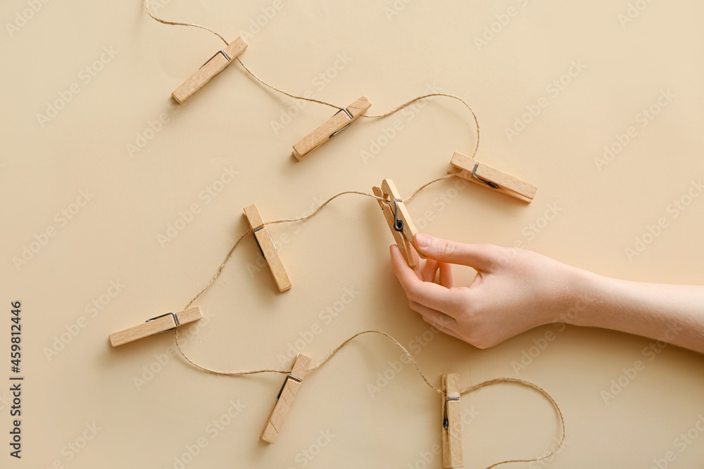 Female hand with clothespins and rope on beige background