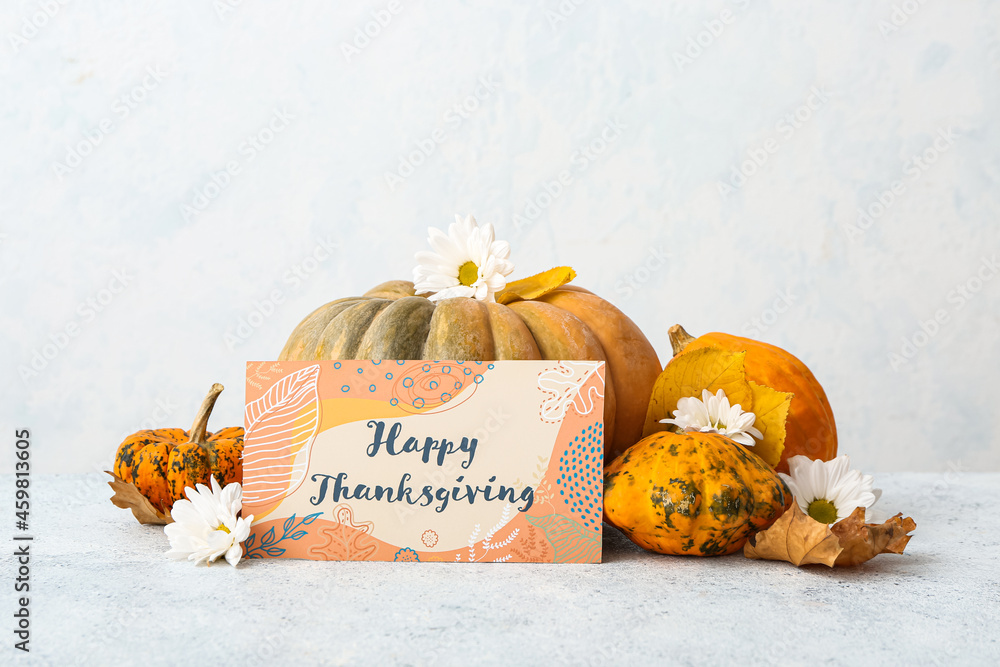 Different pumpkins, flowers and text HAPPY THANKSGIVING on light background