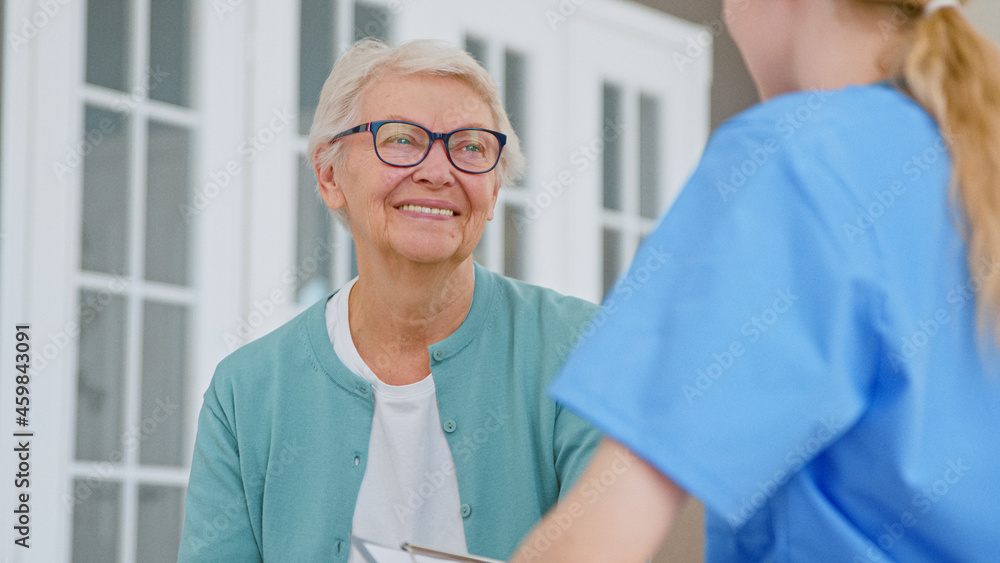 Positive senior lady nods head listening to caregiver recommendations in light office