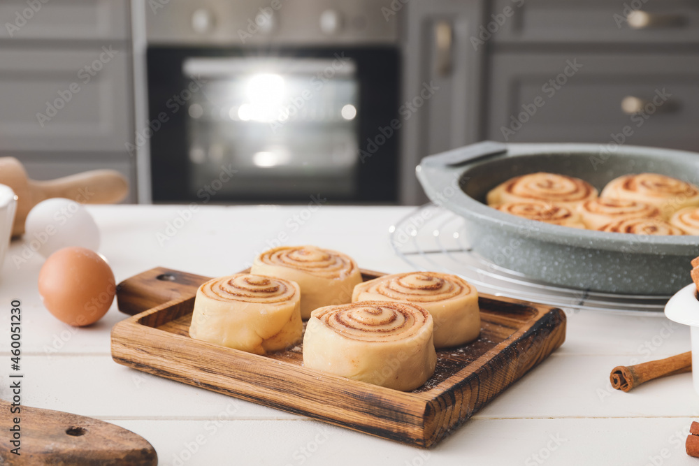 Board with uncooked cinnamon rolls on table in kitchen