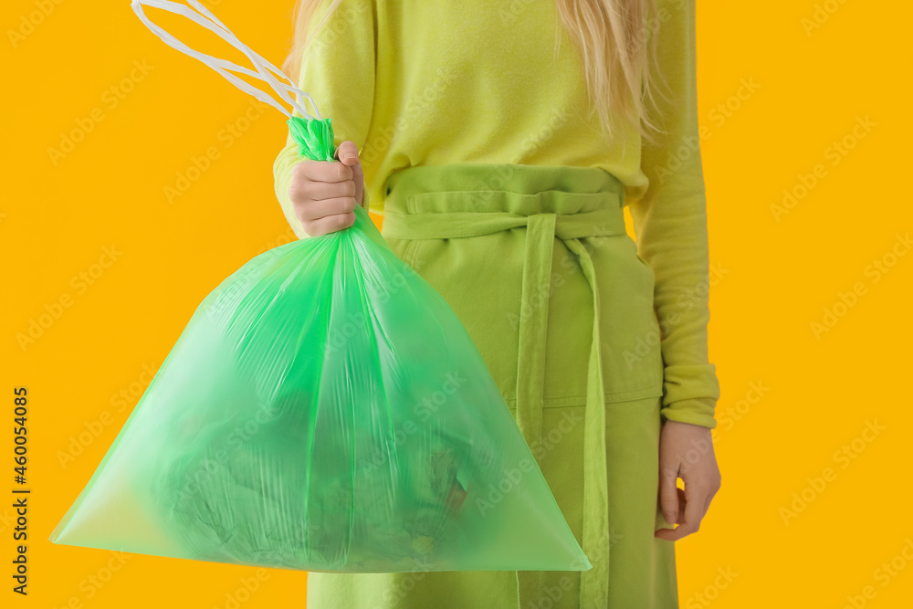 Woman holding bag with garbage on color background, closeup