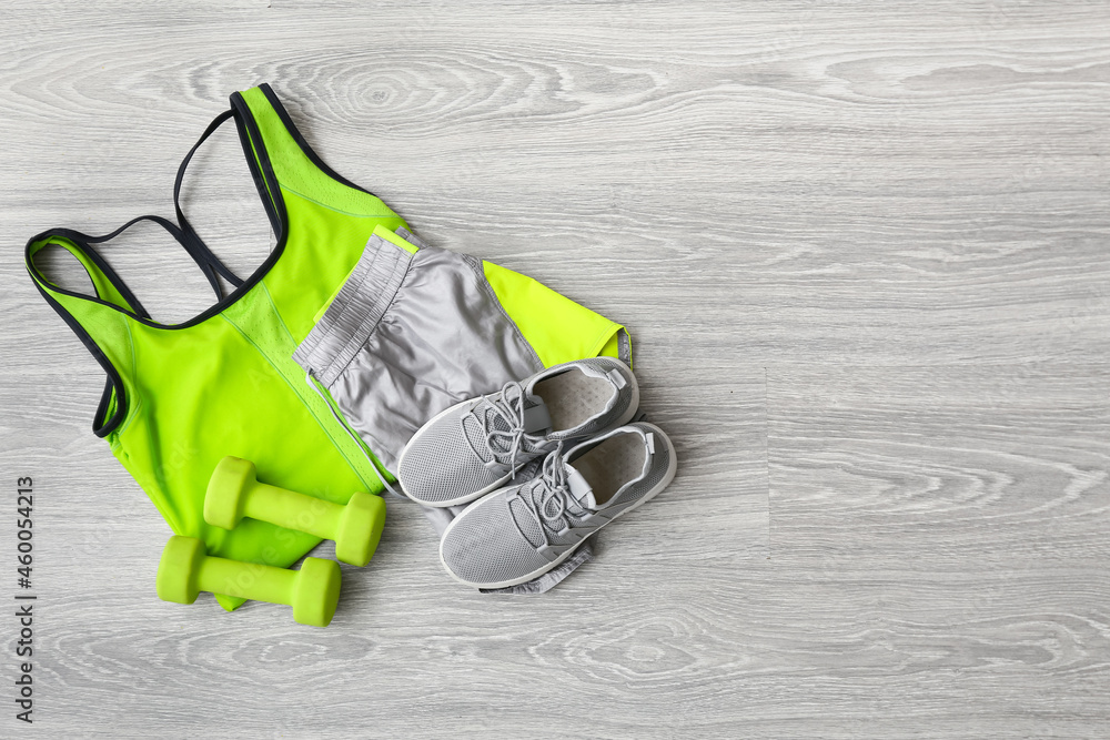 Sportswear, shoes and dumbbells on light wooden background