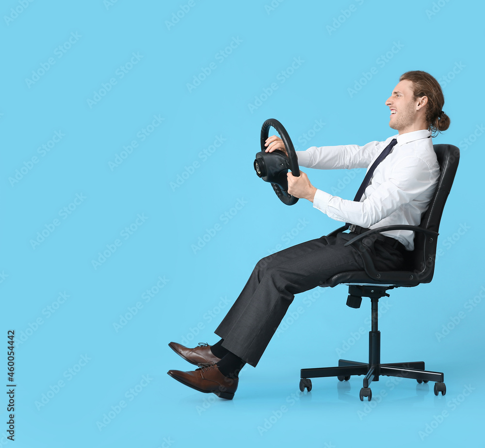 Young man with steering wheel sitting on chair against color background