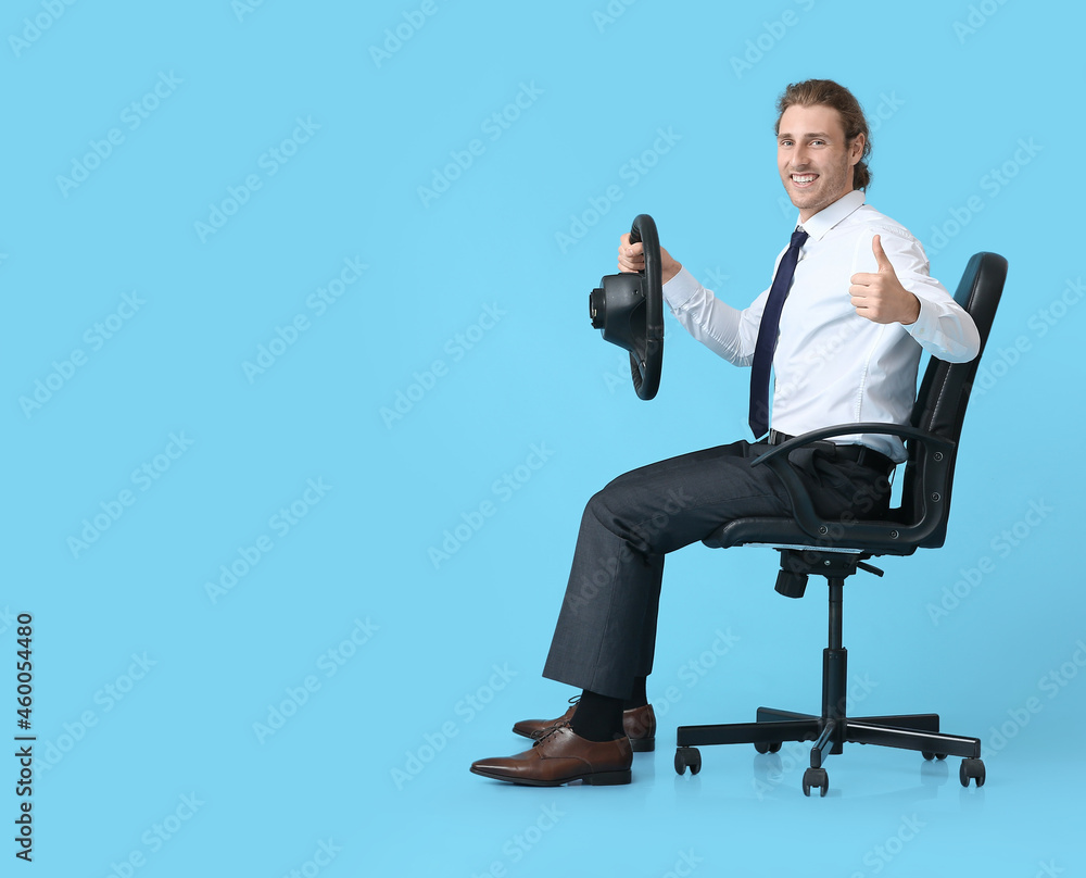 Young man with steering wheel showing thumb-up on color background