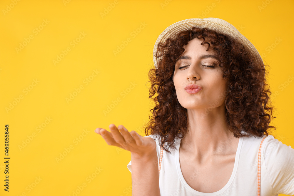 Young beautiful woman in boater hat sending air kiss on yellow background