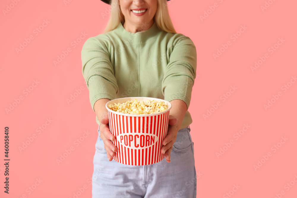 Mature woman with tasty popcorn on color background