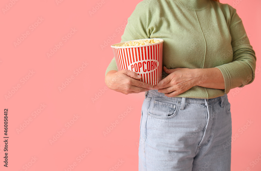 Mature woman with tasty popcorn on color background