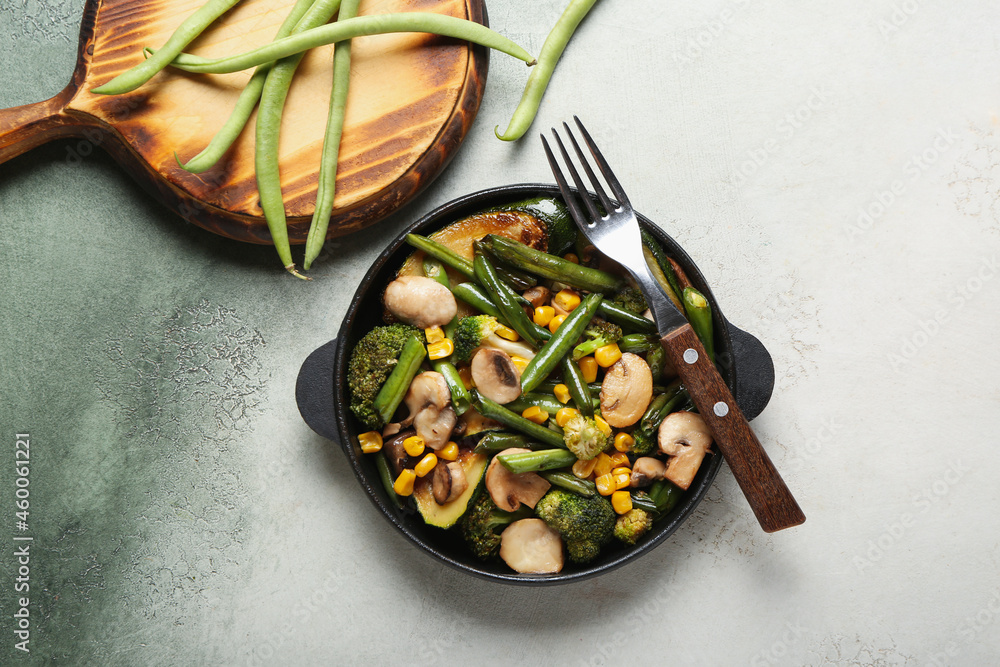 Frying pan with different vegetables on color background