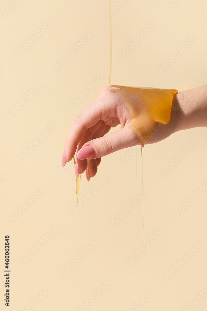 Pouring of honey onto female hand on color background, closeup