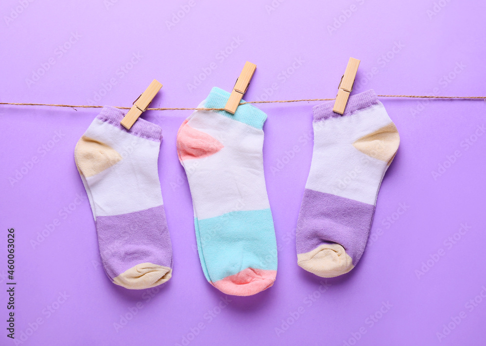 Different socks hanging on rope against lilac background