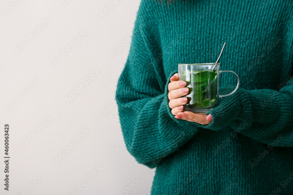 Woman with cup of tasty mint tea on light background, closeup