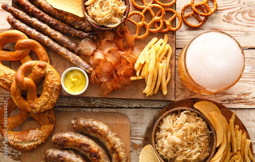 Glass of cold beer, board with Bavarian sausages and snacks on white wooden background. Oktoberfest 