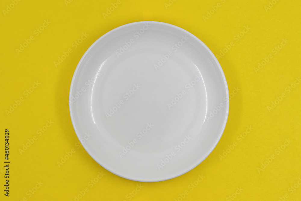 Table setting, empty white plate on yellow background, photo directly above