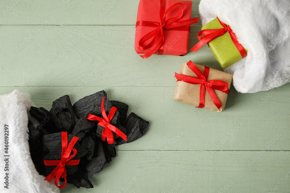 Christmas socks with coal and gift boxes on color wooden background