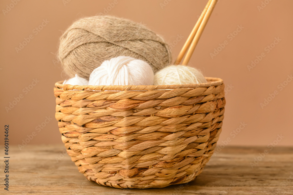 Wicker basket with knitting yarn and needles on wooden table against color background