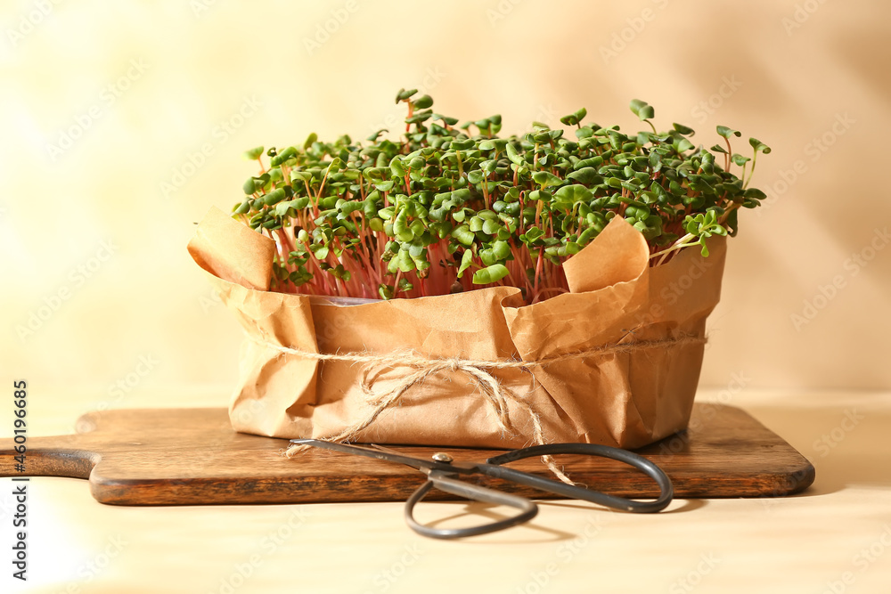 Wooden board with fresh micro green and scissors on color background