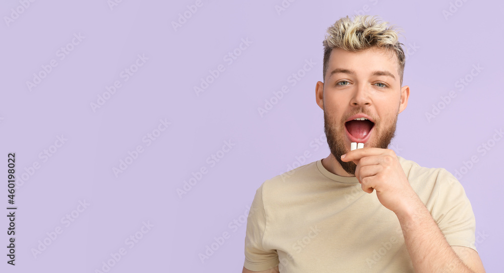 Young man with chewing gum on color background