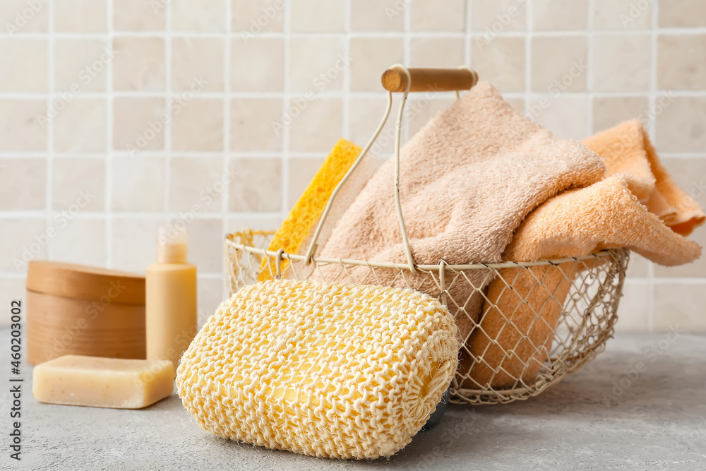 Loofah sponge with bath products and basket with towels on table