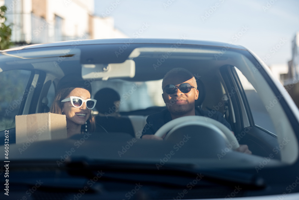 Multiracial couple riding together in car. Young european woman holding groceries after shopping. Co