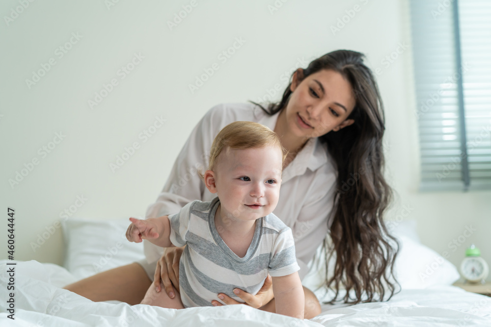 高加索母亲在家里的床上与可爱的男婴玩耍。