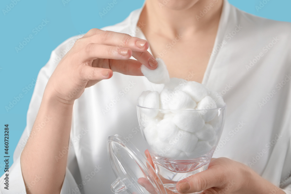 Beautiful young woman with cotton wool on color background, closeup