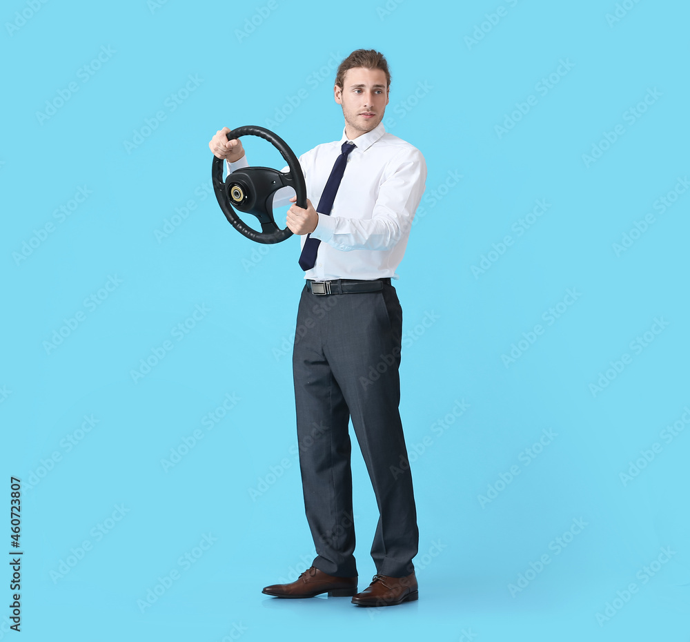 Young man with steering wheel on color background