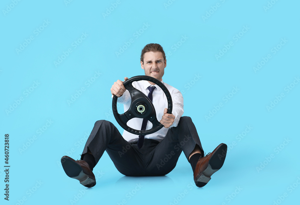 Young man with steering wheel on color background