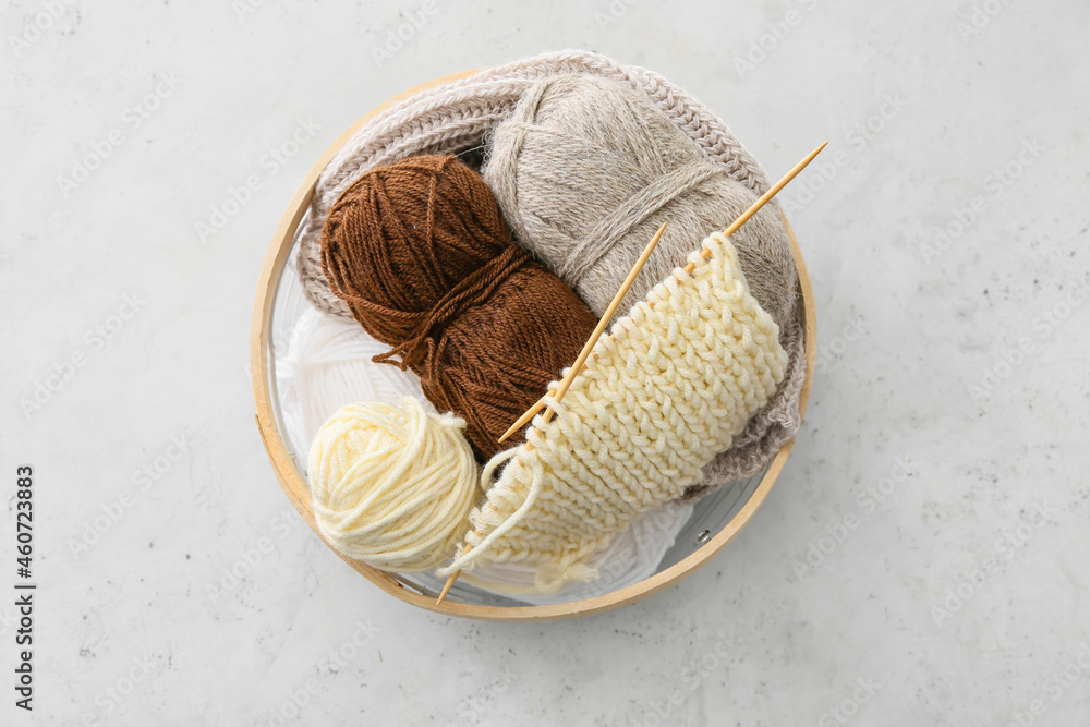 Basket with knitting yarn and needles on light background