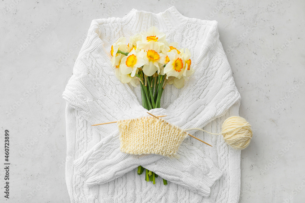 Composition with knitting yarn, needles, sweater and flowers on light background