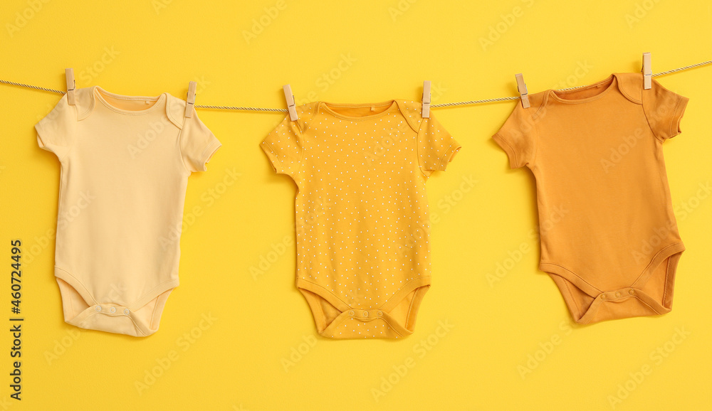 Stylish baby clothes hanging on rope against yellow background