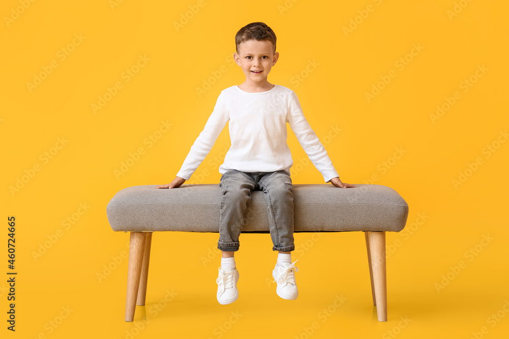 Portrait of cute little boy sitting on bench against color background