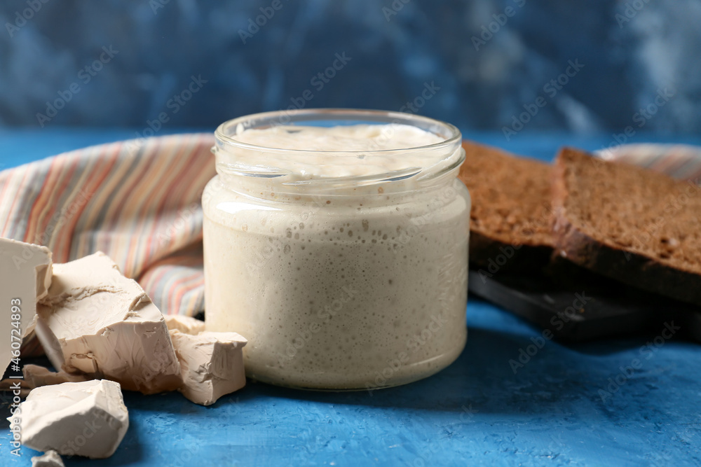 Glass jar with sourdough on blue background